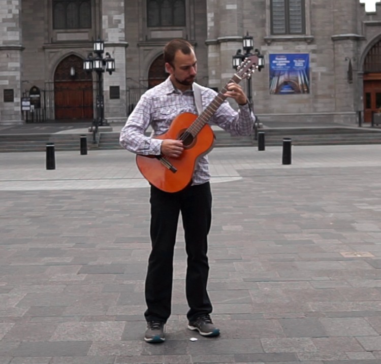 Expert guitarist Brett Vachon playing a classical guitar in a public square.